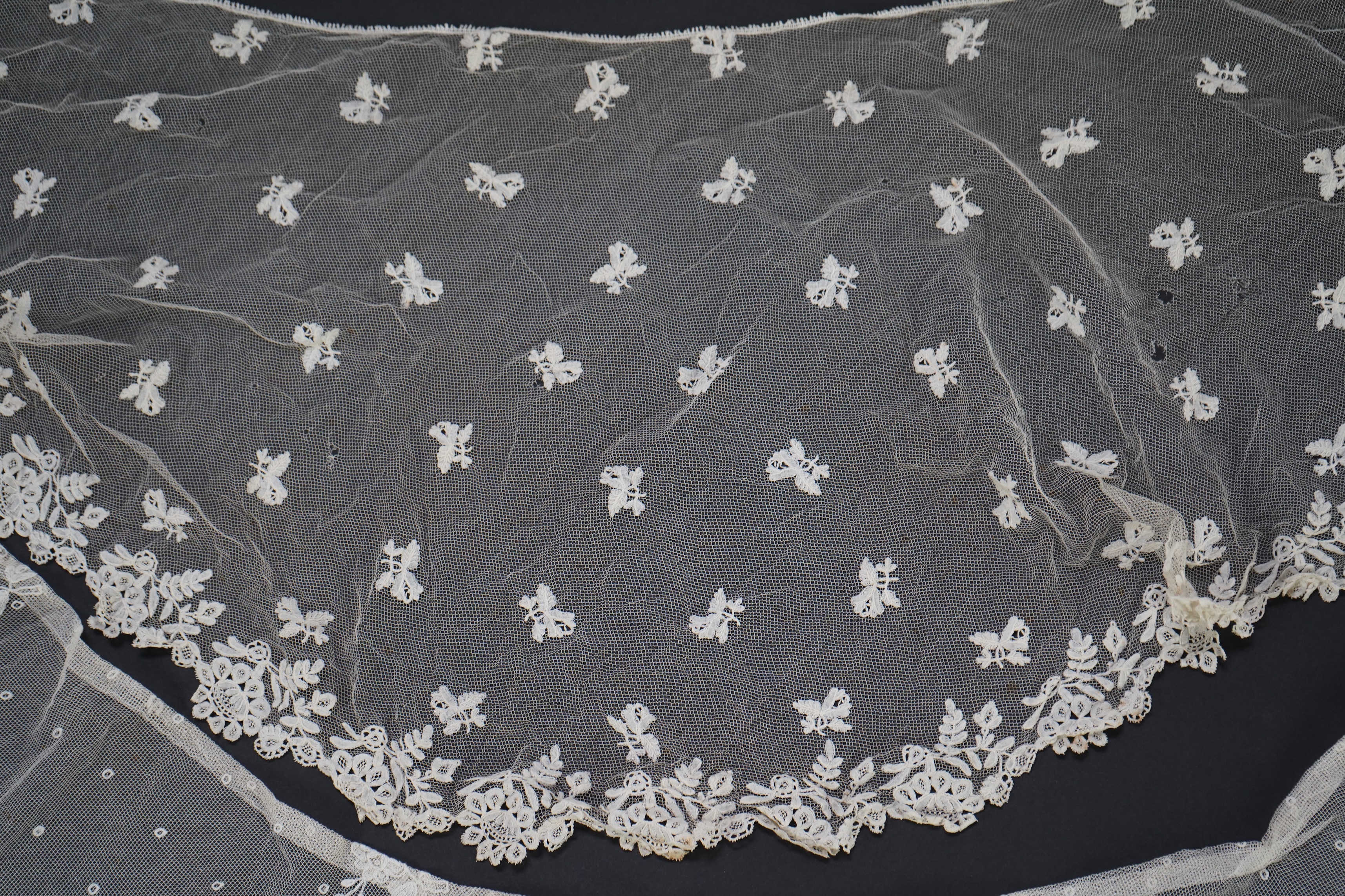 A white tape lace on net bed cover, a cream lace needle run panel, three Brussels bobbin lace collars, a lappet and two beaded tea pot covers, bed cover 200cm x 250cm. Condition - the bedcover has damage to the netting,